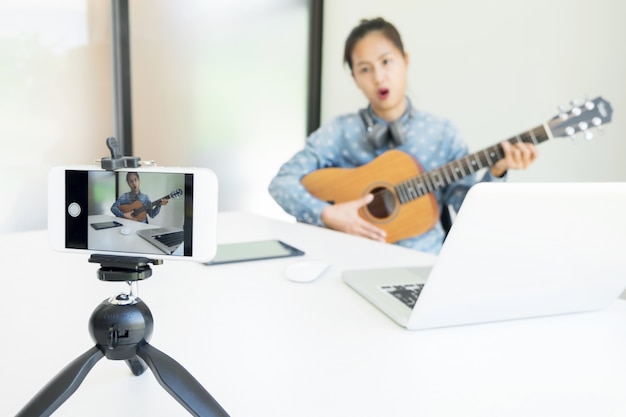 Vrouwen zingen een liedje met gitaar in handen, gebruik camera om live video naar sociaal netwerk uit te zenden via internet thuis.