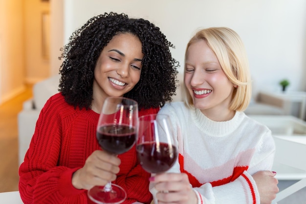 Vrouwen zitten op de bank en lachen in een gezellig loft met wijn Twee vrouwelijke vrienden ontspannen zich op de bank thuis met een glas wijn praten samen