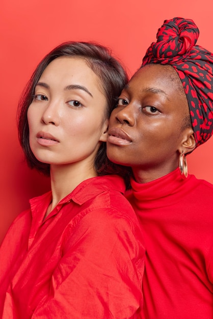 vrouwen, zussen of vrienden staan dicht naast elkaar, kijken serieus naar de camera gekleed in felrode kleding poseren binnenshuis hebben een gezonde schone huid. Vrouwelijk concept