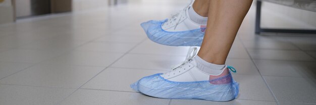 Vrouwenbenen in sneakers met schoenovertrekken in ziekenhuisgang