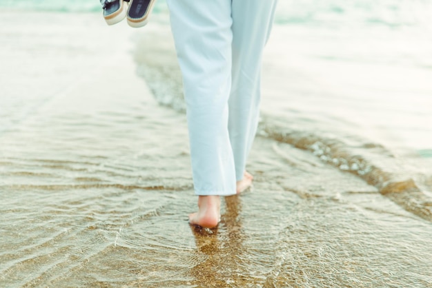 Vrouwenbenen in witte broek die door zeestrand lopen