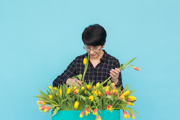 Vrouwenbloemist op middelbare leeftijd met houten doos van tulpen op blauw