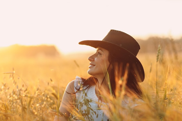 Vrouwenboer in het profielportret van de cowboyhoed bij landbouwgebied op sunset