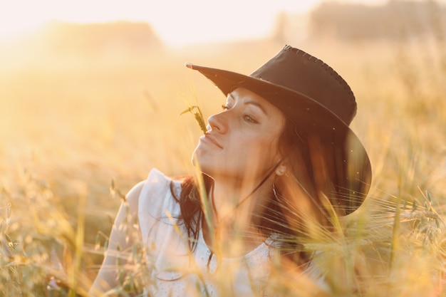 Vrouwenboer in het profielportret van de cowboyhoed met oor bij landbouwgebied op sunset