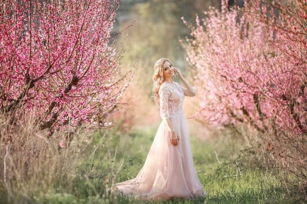 Vrouwenbruid op huwelijksdag alleen in lange roze kleding in tot bloei komende tuin