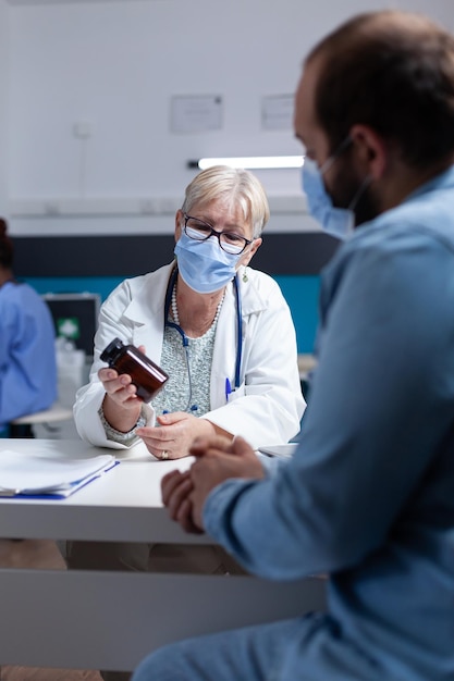 Vrouwendokter die fles pillen toont aan patiënt voor helende behandeling bij controlebezoek. Arts die een pot met medicijnen vasthoudt om een antibioticum op recept aan de man te geven bij een onderzoeksafspraak.