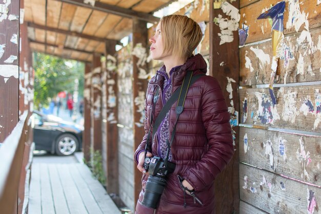Vrouwenfotograaf met een camera op een houten achtergrond in een warme jas in de herfst