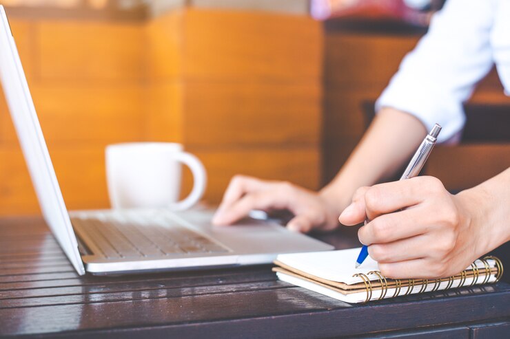 Vrouwenhand die aan een notitieboekjecomputer werken en met een pen op blocnote schrijven.