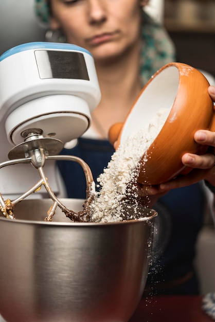 Vrouwenhand die bloem op kom van een elektrische mixer zet voor de voorbereiding van het zelfgemaakte Argentijnse alfajores-recept