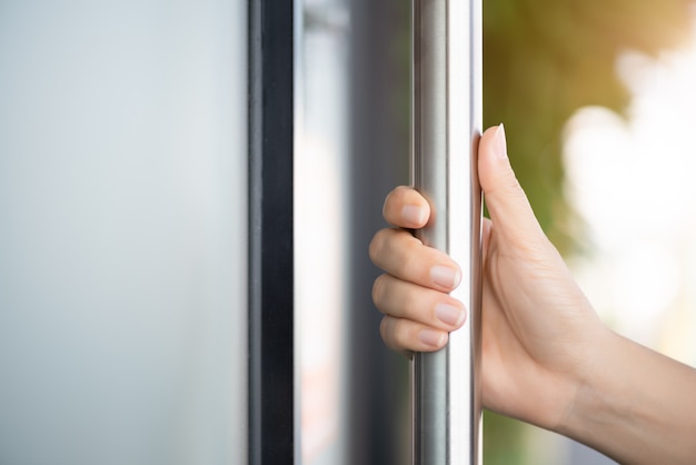 Vrouwenhand die de deurbar houden om de deur met de achtergrond van de glasbezinning te openen.