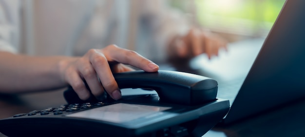 Vrouwenhand die de telefoon houden en laptop op het bureau werken.