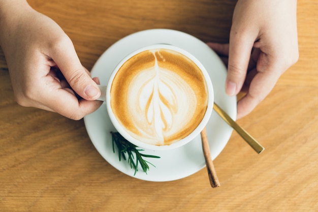 Vrouwenhand die een witte koffiemok houden. Koffie is een latte. tafel op de houten