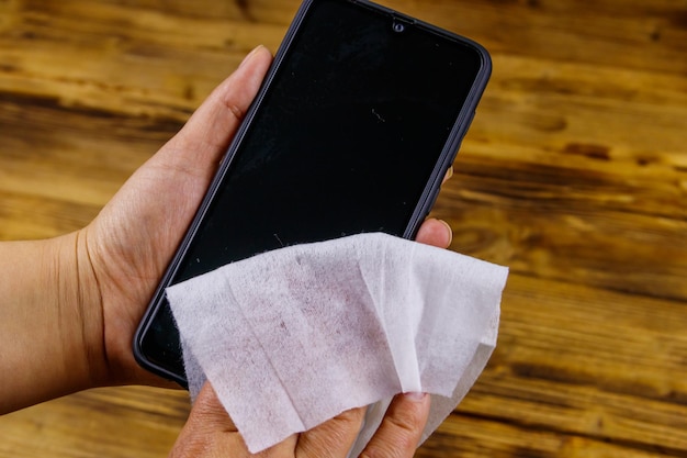 Vrouwenhand die het smartphonescherm schoonmaakt met een nat doekje