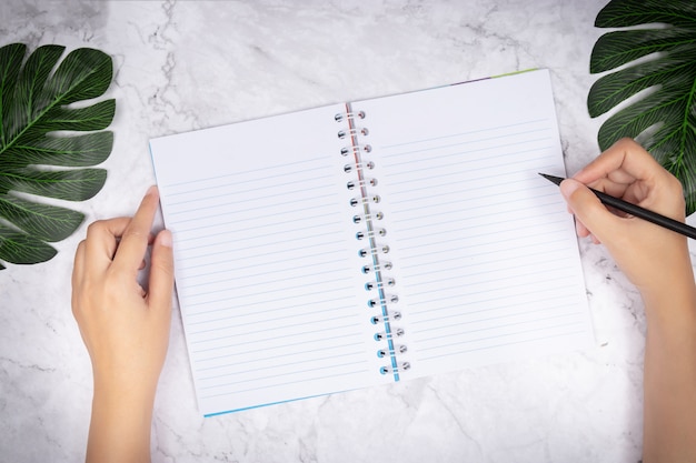 vrouwenhand die in een leeg wit paginanotitieboekje op wit marmeren bureau schrijven