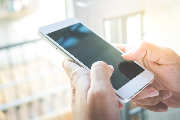 Vrouwenhand die mobiele slimme telefoon met het lege scherm in een moderne stijlwoonkamer houden.