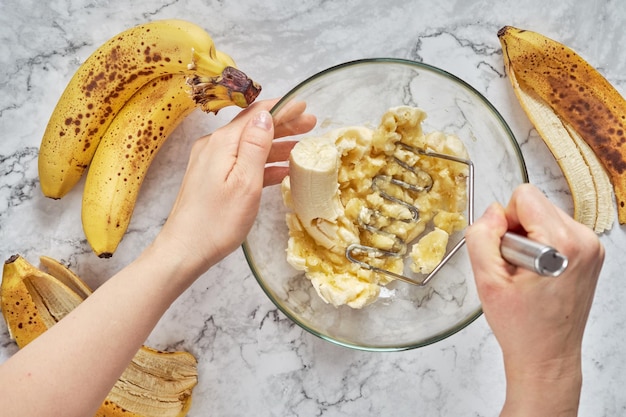 Vrouwenhand die verschillende bananen fijnmaakt om in een bananenbrood te bakken