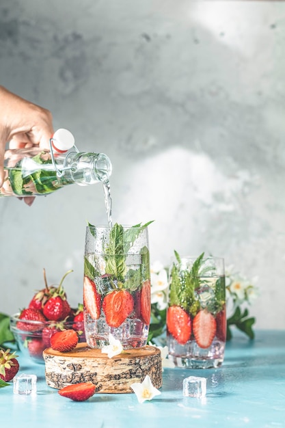 Vrouwenhand giet detoxwater van glazen fles naar glas met aardbeienijs en munt Zomerverse Mint frisdrankcocktail selectieve focus