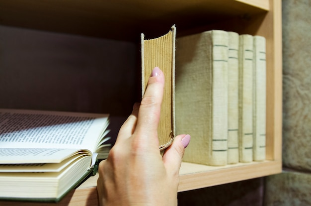 Vrouwenhand kies het juiste boek van de plank met boekencollectie voor studie