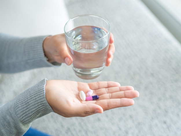 Vrouwenhand met de tabletten van de pillengeneeskunde en glas water