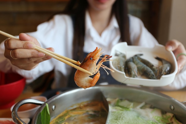 Vrouwenhand met eetstokjes verse garnalen met groenten om te koken of shabu shabu