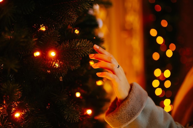 Vrouwenhand met kerstverlichting aan de boom. Feestelijke kerstmarkt, wintervakantie concept.