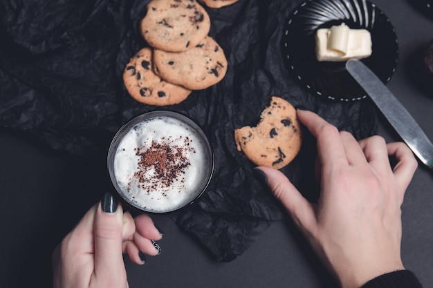 Vrouwenhand met kop koffie of cappuccino en chocoladekoekjes, koekjes