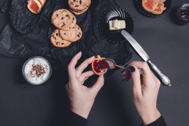 Vrouwenhand met lepel met jam en koekjes dichtbij kop van koffie of cappuccino