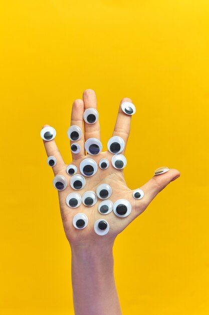 Vrouwenhand met plastic ogen en gebaar van vingers op een gele achtergrond, kopieer ruimte. gebarentaal concept.