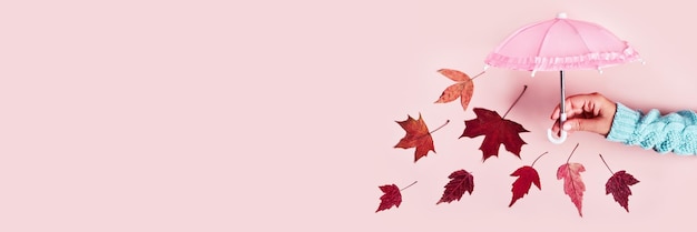 Vrouwenhand met roze paraplu en vallende bladeren op roze pastelachtergrond Hallo herfst creatief concept