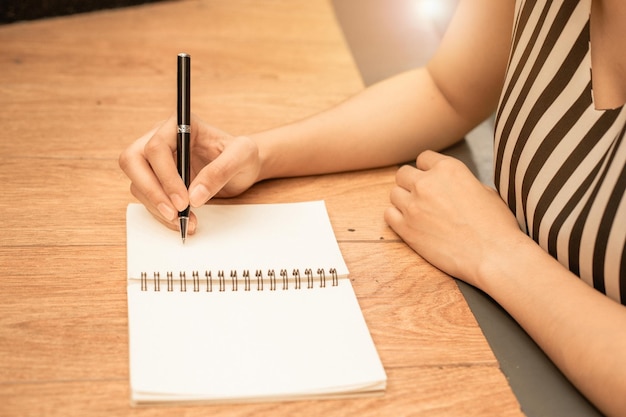 Foto vrouwenhand schrijft op een leeg notitieblok met een pen op houten achtergrond