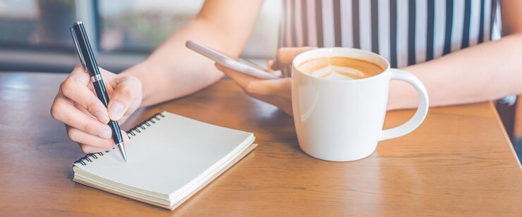 Vrouwenhand schrijft op een notitieblok met een pen op een houten bureau en houdt een mobiele telefoon vast
