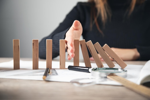 Foto vrouwenhand voorkomt dat houten dominostenen op houten huismodel vallen