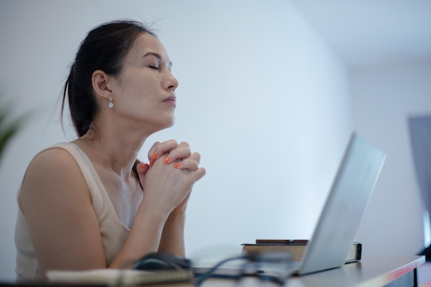 Vrouwenhanden bidden thuis met kruisbijbel en laptop