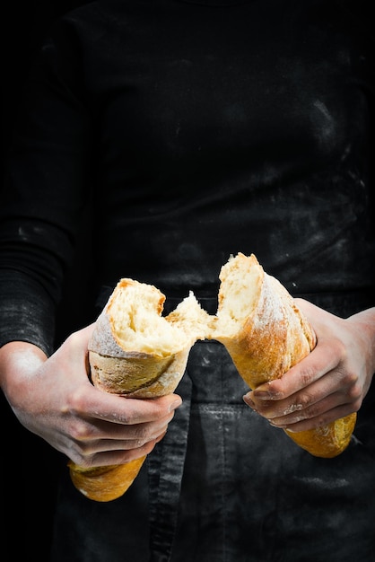 Vrouwenhanden breken het stokbrood geïsoleerd op zwarte achtergrond