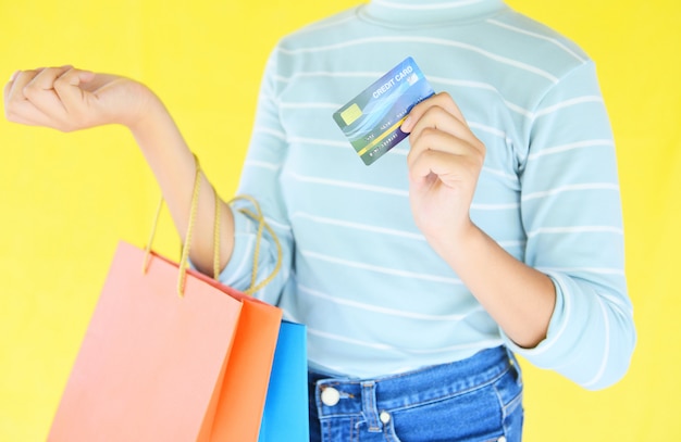 Vrouwenhanden die creditcard houden en het winkelen zak op gele achtergrond houden.