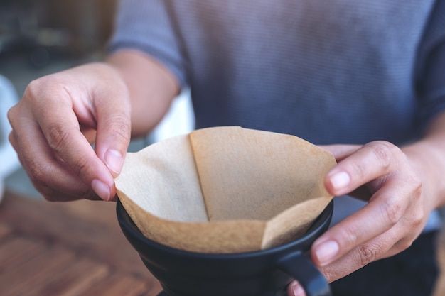 Vrouwenhanden die een filter plaatsen om een infuuskoffie op uitstekende houten lijst te maken