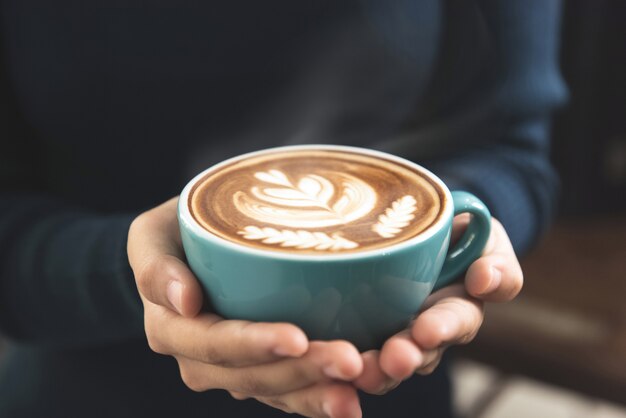 Vrouwenhanden die een kop van de koffie van de lattekunst geven