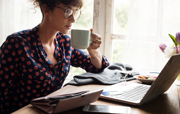 Vrouwenhanden die koffiekop houden die aan laptop werken