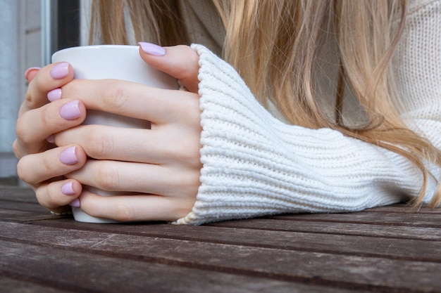 Vrouwenhanden die kop van koffie of theemok op houten lijst houden.