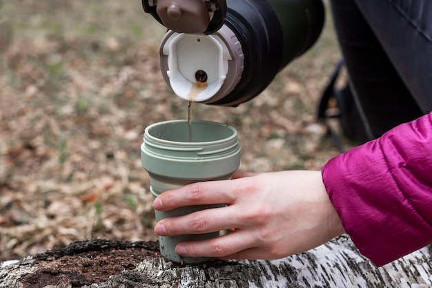 Foto vrouwenhanden die thee uit thermos in beker gieten warme drankpauze tijdens wandelen of kamperen in de herfst of lente