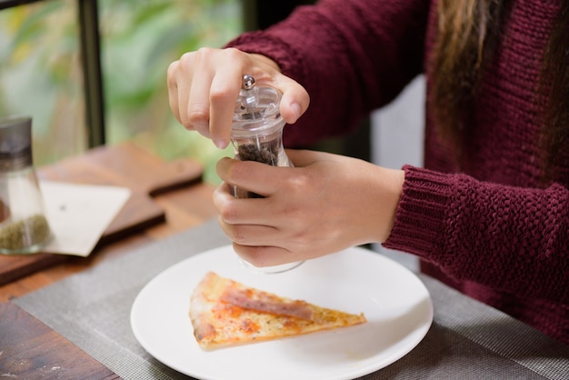 Vrouwenhanden die zwarte peper en zoute schudbeker op de plakken van pizza gebruiken.