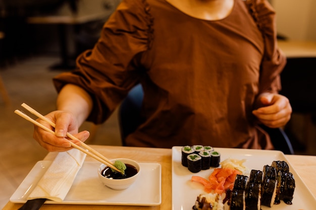 Foto vrouwenhanden gebruiken vakkundig chopsticks voor wassabi. tafel van de sushibar is gedekt om te eten