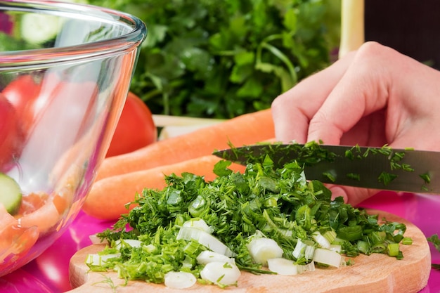 Vrouwenhanden gehakte groene ui en groene dille op een houten bord in de keuken