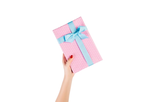 Vrouwenhanden geven ingepakt kerstcadeau of ander handgemaakt cadeau in roze papier met blauw lint. Geïsoleerd op een witte achtergrond, bovenaanzicht. Thanksgiving Geschenkdoos concept.