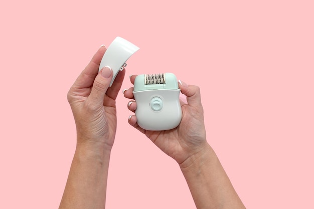 Vrouwenhanden houden een blauwe epilator in hun handen op een roze achtergrond