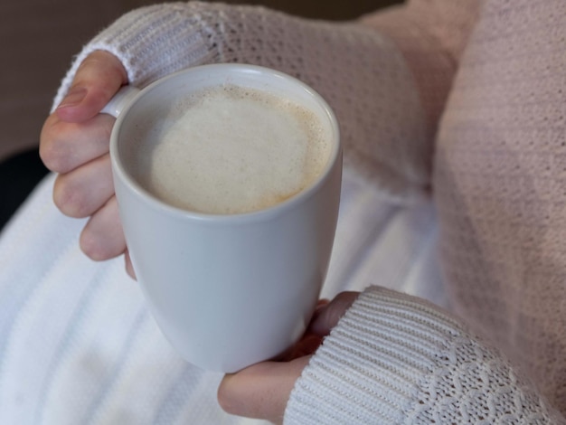 Vrouwenhanden in een warme gebreide trui met een witte mok cappuccino warmte comfort zicht op top