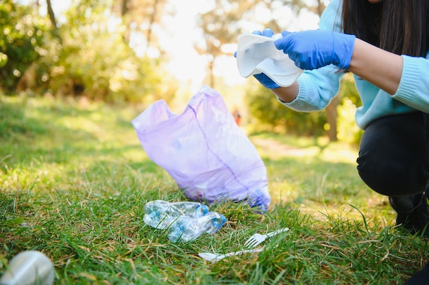 Vrouwenhanden in rode rubberen handschoenen. Vrouw verzamelt afval in de zak. Vrijwilligers ruimen afval op in het zomerpark. Aardige vooruitstrevende vrouw die zich inspant om het milieu te helpen