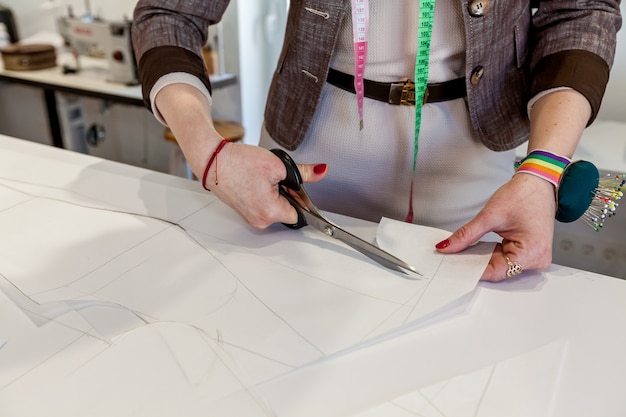 Vrouwenhanden knippen het patroon uit papier met een kleermakersschaar op een witte tafel