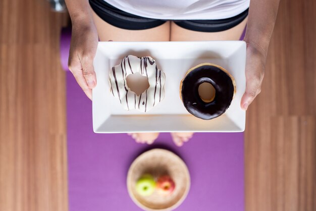 Vrouwenhanden met gebakken donut tijdens het staan op yogamat, gezond dieet, dieetconcept, bovenaanzicht