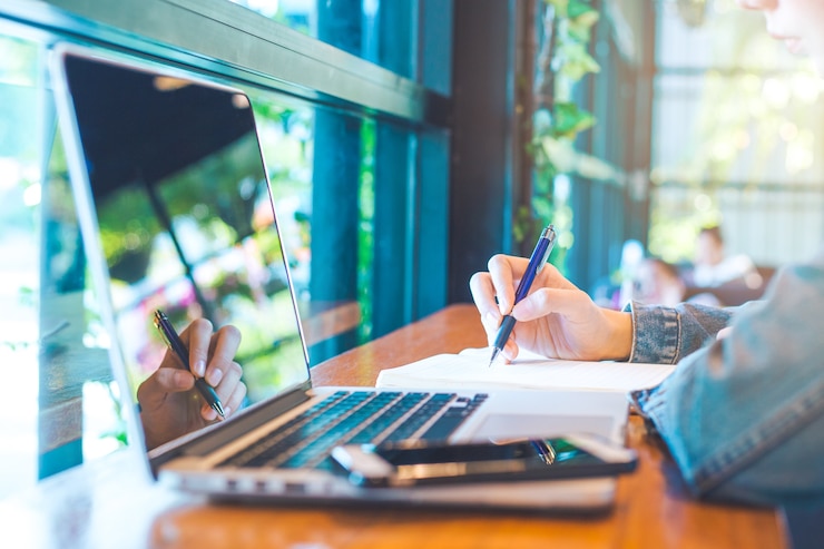 Vrouwenhanden met pen die op notitieboekje in het bureau schrijven.
